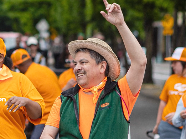 CareOregon Employee in a Green vest and orange t shirt waving his hand at a parade.